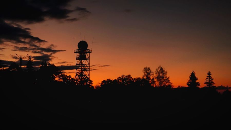 Silhouette trees and tower against sky during sunset