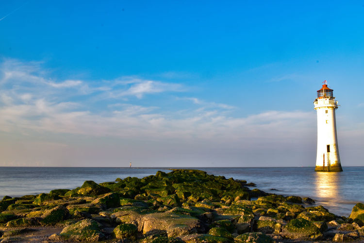 Lighthouse amidst sea and buildings against sky