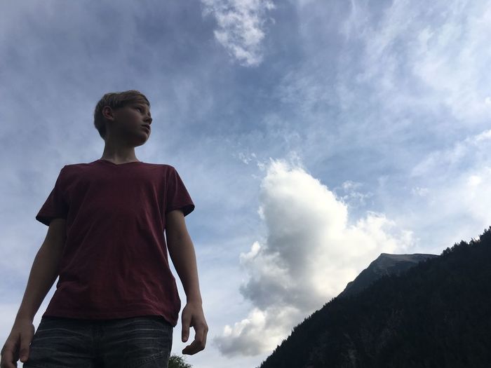 Low angle view of young boy standing against blue sky