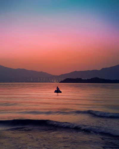 Silhouette person in sea against orange sky