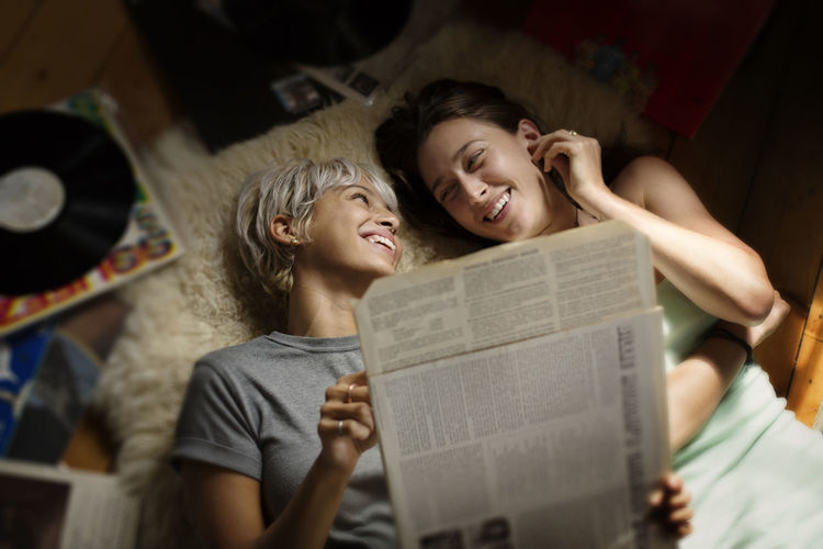 Overhead view of happy woman holding vinyl record while lying with friend on floor