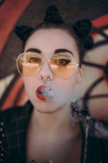 Close-up portrait of young woman smoking cigarette by graffiti wall