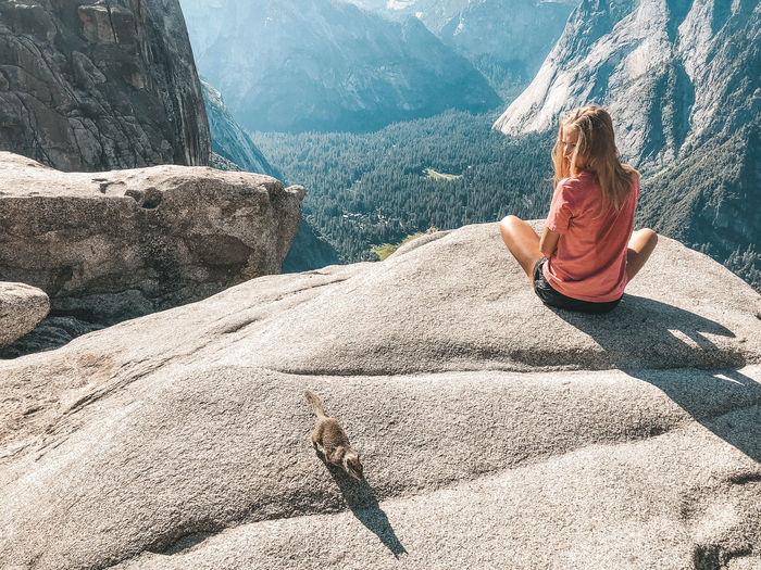 Rear view of woman looking at squirrel while sitting on rock