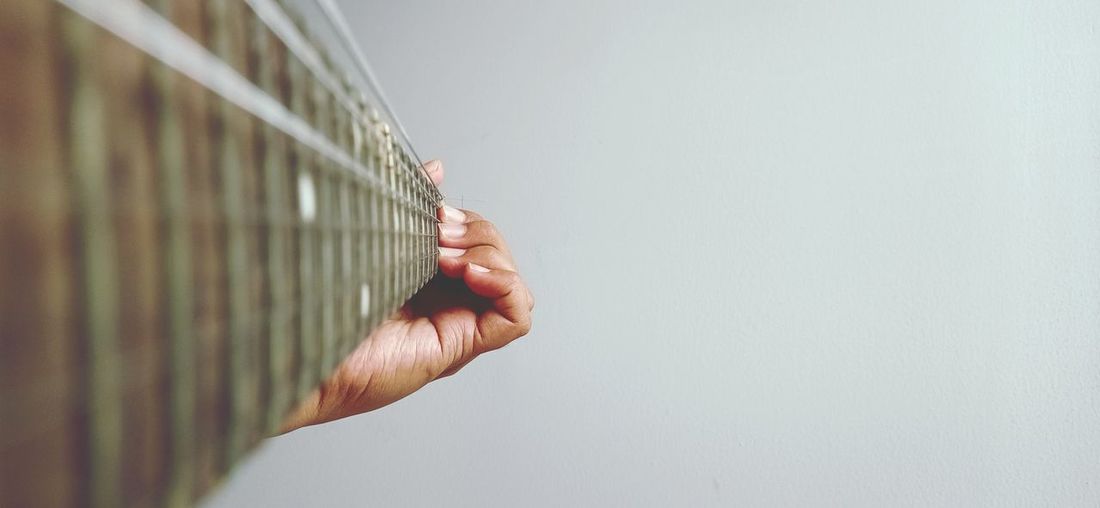 Close-up of hand holding guitar against wall