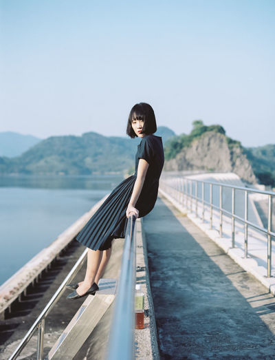 Woman sitting on walkway railing against clear sky