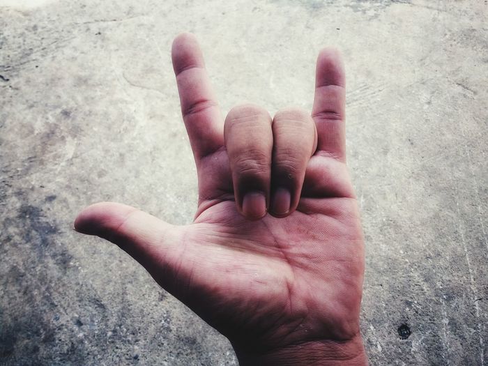 Close-up of hand showing horn sign against wall