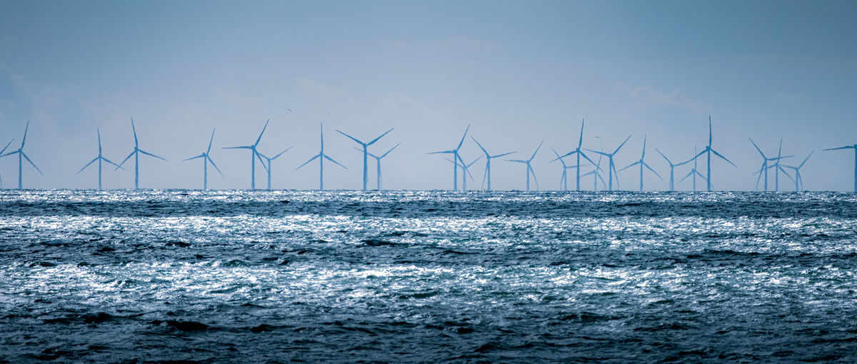 Wind turbines on sea shore against sky