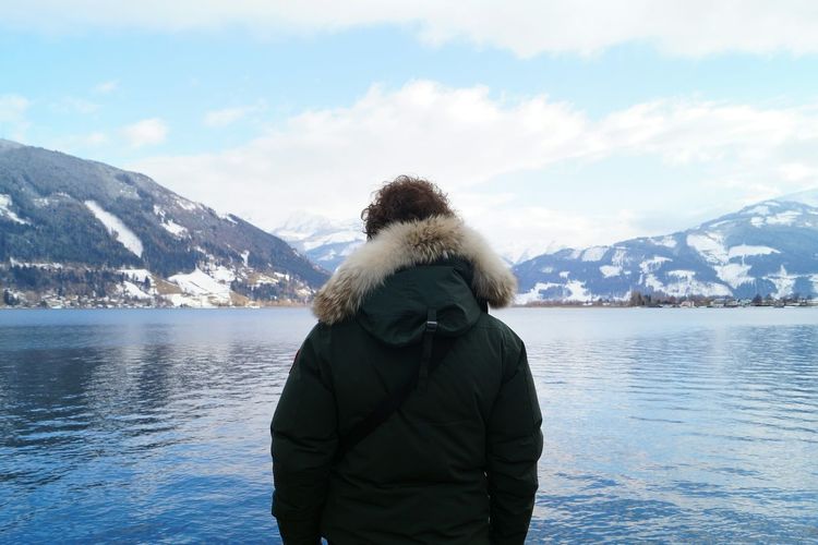 Rear view of man standing at lakeshore against sky