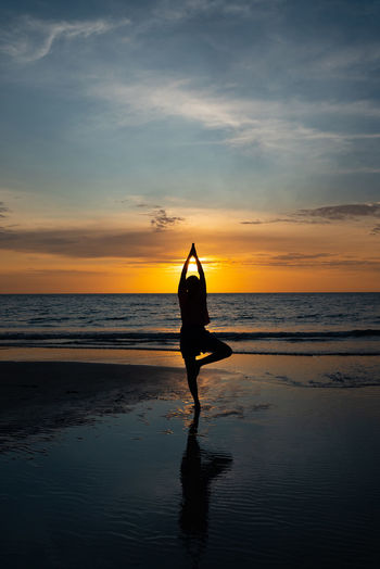 Silhouette woman standing at beach against sky during sunset