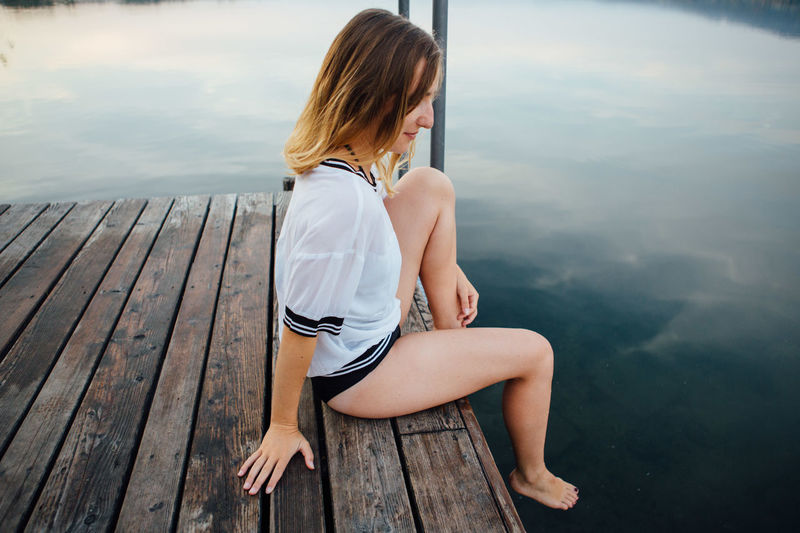 Young woman sitting on pier by lake