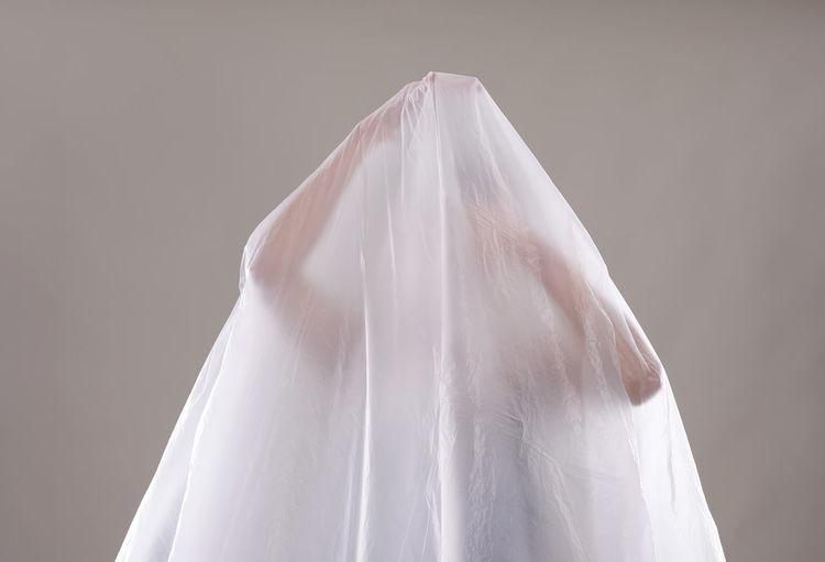 Woman covered in white textile over white background