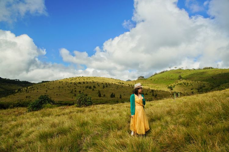 Mid adult woman standing on green landscape against sky