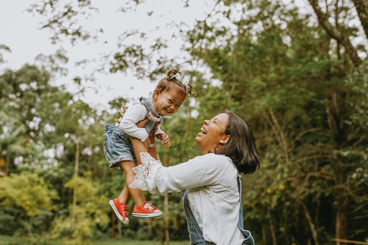 Side view of mother holding daughter mid air while standing at park