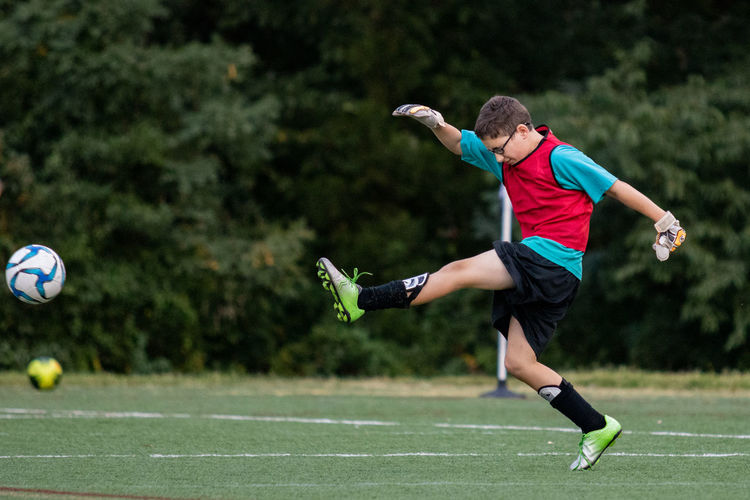 Full length of boy kicking soccer ball on grass in a game