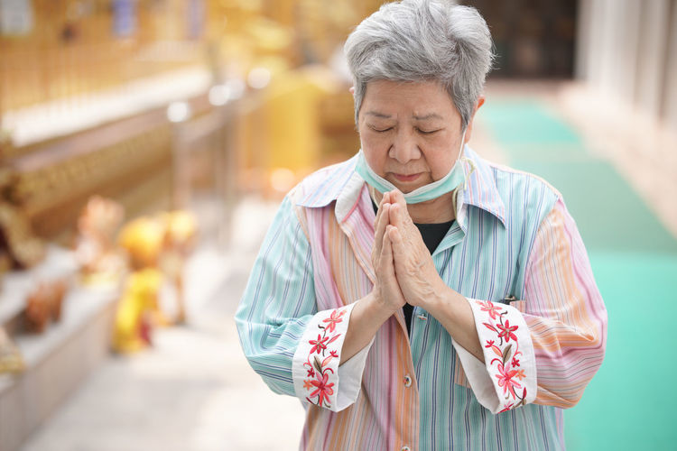 Old asian elder senior woman traveler tourist praying at buddhist temple.