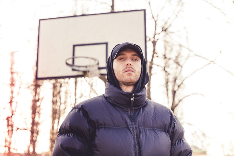 Portrait of young man standing against basketball hoop and trees