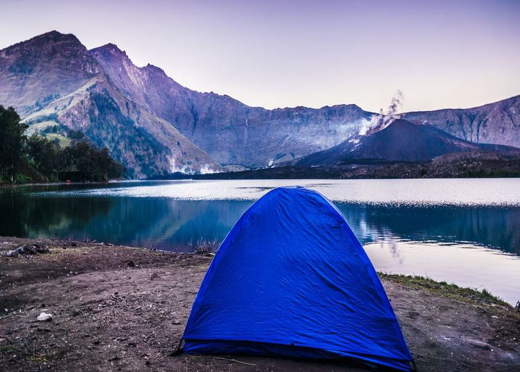 Tent at lakeshore by mountains against sky