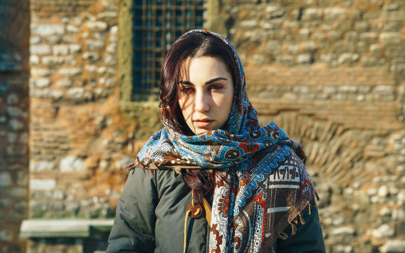 Portrait of young woman wearing scarf while standing outdoors during sunny day
