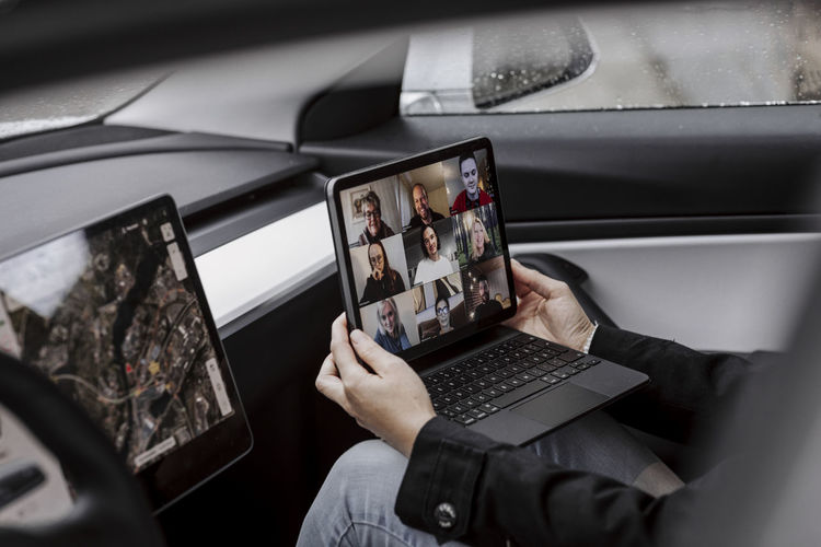 Woman in car holding laptop with video conference