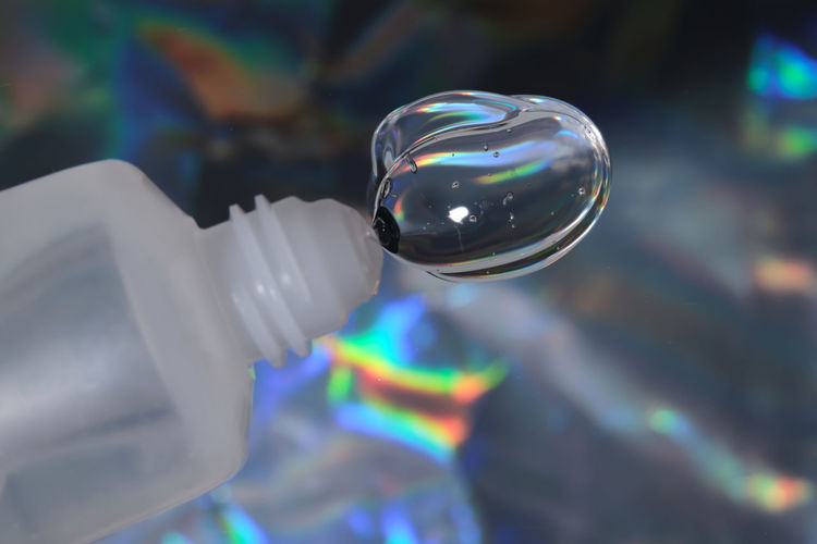Hyaluronic gel or shower gel squeezed out of a bottle on a holographic background.