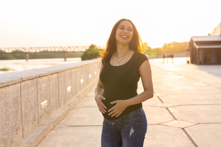 Smiling young woman standing on bridge against sky