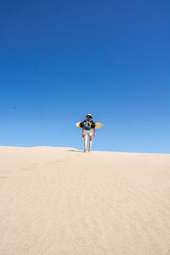 Man standing on sand dune in desert against clear blue sky