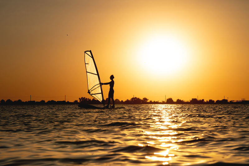 Woman windsurfer silhouette at lake sunset. beautiful beach landscape. summer water sports 