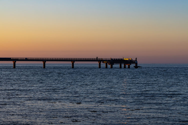 Silhouette pier over sea against sky during sunset