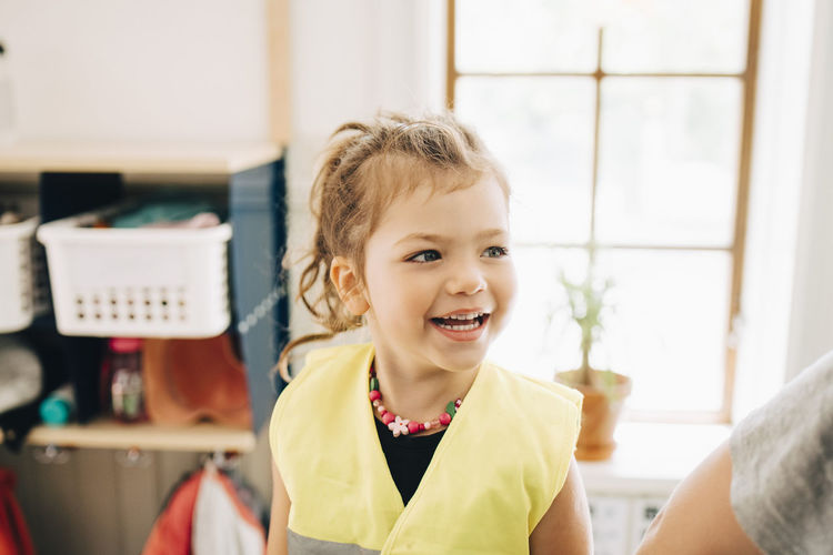 Smiling girl looking away while standing in cloakroom at kindergarten