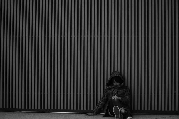 Homeless young woman sitting against corrugated iron