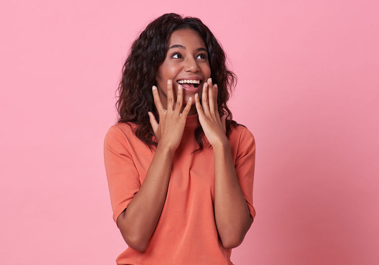 Beautiful young woman laughing against pink background