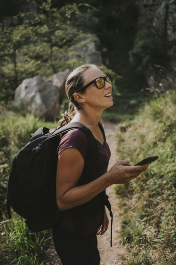 Woman looking away while holding smart phone for navigation during hiking on sunny day