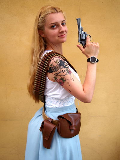 Portrait of beautiful woman holding gun while standing against wall