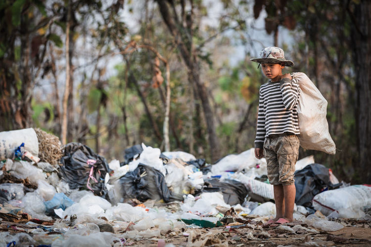 Boy holding plastic bag while standing at dump yard