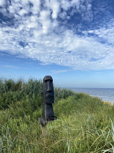 Wooden post on field by sea against sky