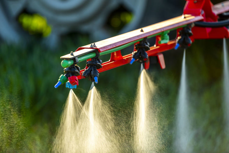 Close-up of tractor with crop sprayer sprinkling fertilizer in farm