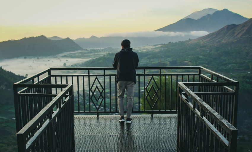 Rear view of man standing on railing against mountains