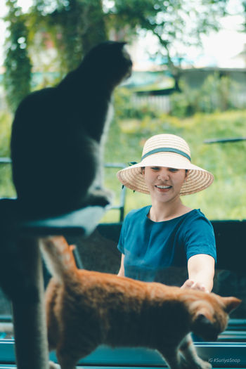 Smiling woman wearing hat playing with cat