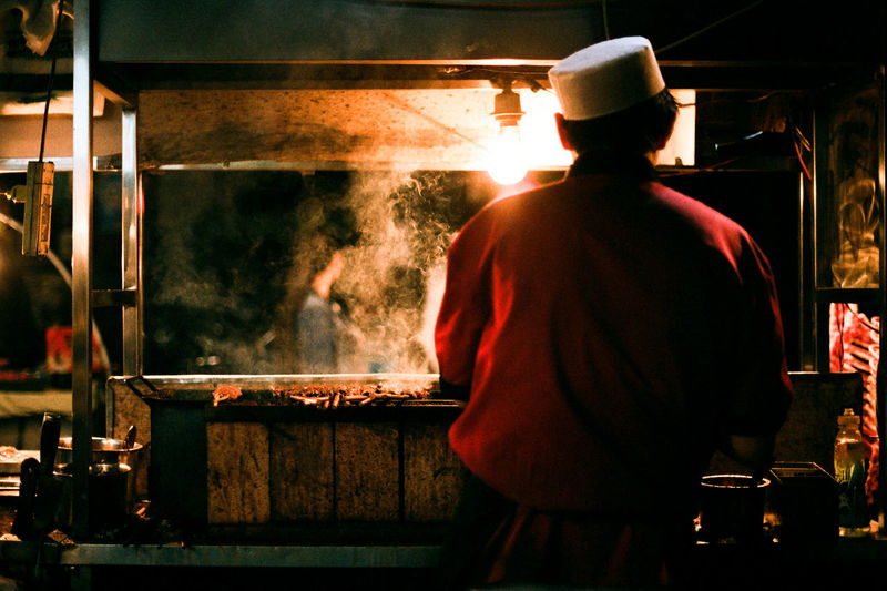 Rear view of man cooking food at market stall