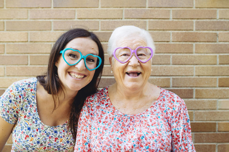 Happy granddaughter and grandmother wearing heart-shaped glasses