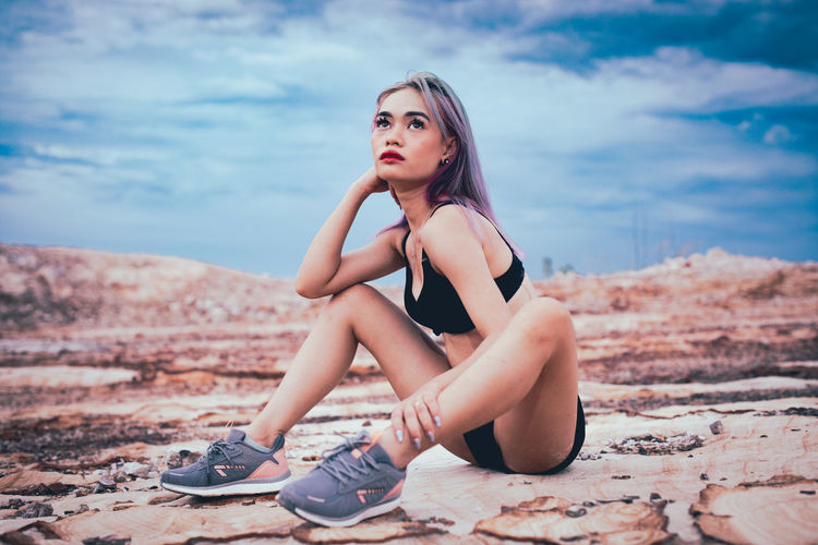 Portrait of beautiful young woman sitting against sky