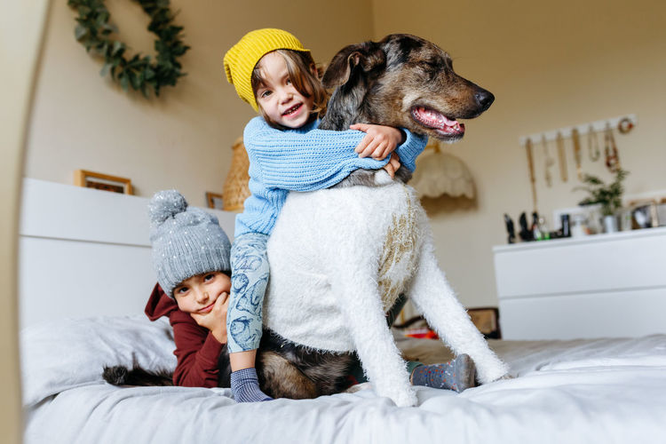 Two children in warm clothes hug their dog