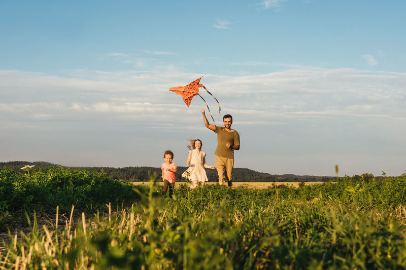 Family running on grassy land against sky