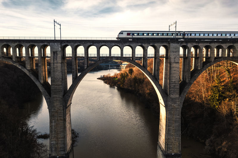 Train on arch bridge over river against sky