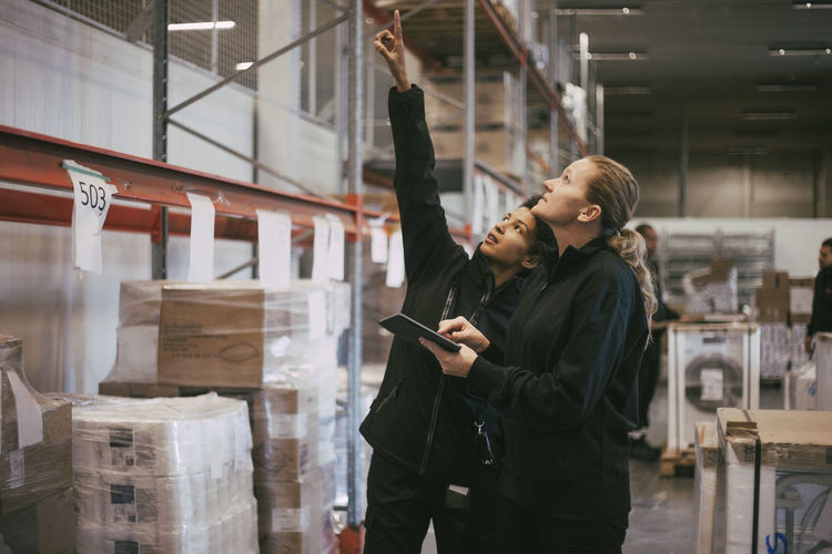 Businesswoman pointing while discussing with female manual worker at warehouse