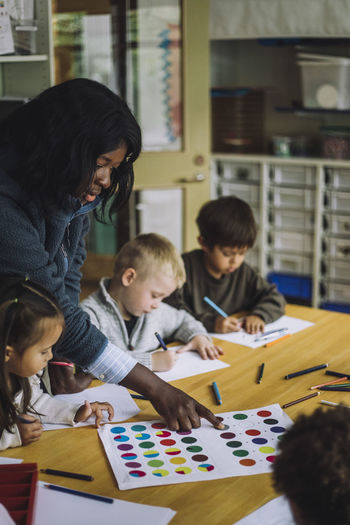 Female teacher guiding students to recognize colors while training them in day care center
