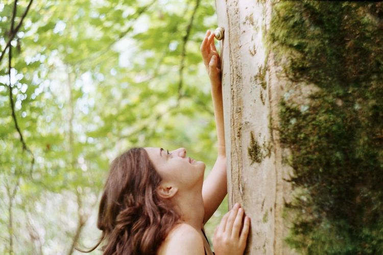 Woman looking up while standing on tree trunk
