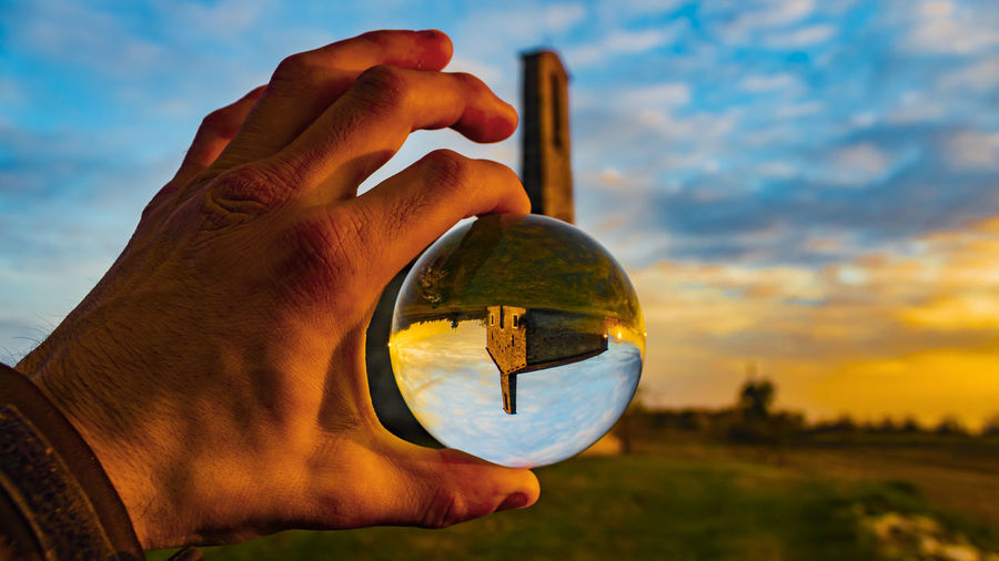Cropped hand holding crystal ball against sky