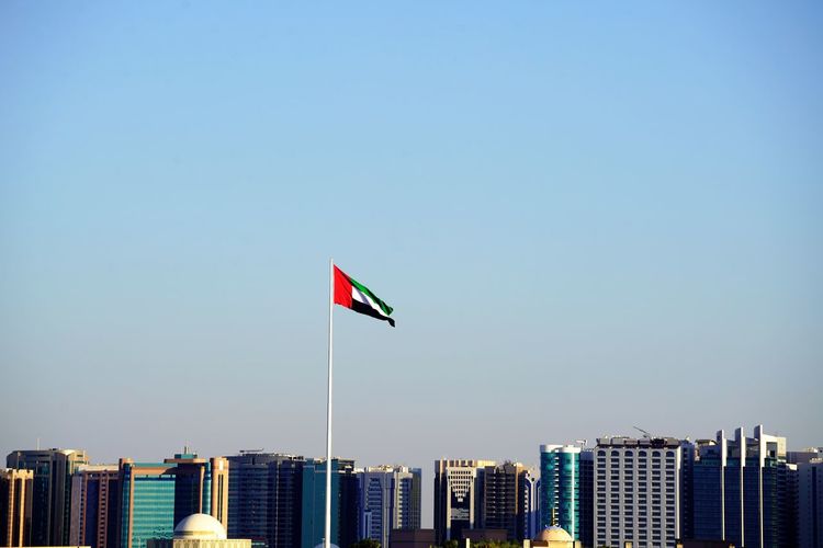 Flag against buildings in city against clear blue sky