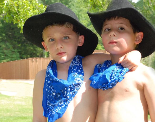 Portrait of shirtless brothers wearing hats in yard